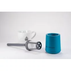 Snadno rozložitelné plastové sítko s modrou nádobkou vhodné pro cestování a v pozadí bílý šálek s logem Lázeňské kávy