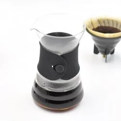 Hario V60 Drip Decanter s černou koženou rukojetí v pozadí papírový filtr s namletou kávou