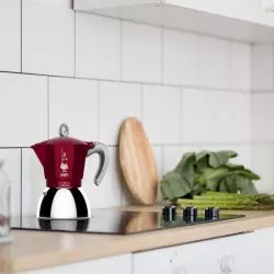 Moka konvička v červené barvě postavená na indukční desce v kuchyni.