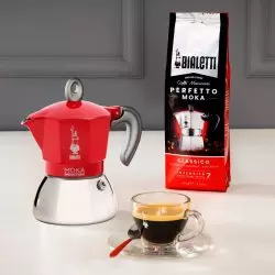 Červená moka konvička od značky Bialetti s kávou a šálkem připraveného espressa.