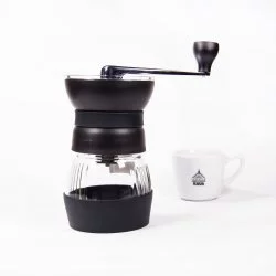 Černý ruční mlýnek Hario Skerton Pro na bílém pozadí s šálkem lázeňské kávy