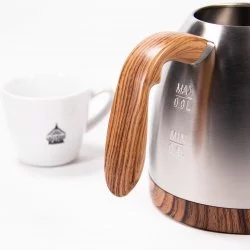 Stříbrná elektrická konvice, detail na dřevěné madlo na bílém pozadí s šálkem lázeňské kávy
