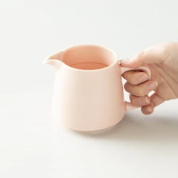 hrnek z porcelánu na filtrovanou kávu v růžové barvě uchopený v rukou.