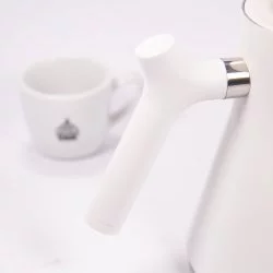 Bílá elektrická konvice, detail na rukojeť konvice, v pozadí šálek lázeňské kávy