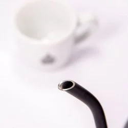 Černá elektrická konvice na bílém pozadí s šálkem lázeňské kávy, detail na husí krk konvice