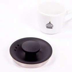 Detail víka černé elektrické konvice na bílém pozadí s šálkem lázeňské kávy