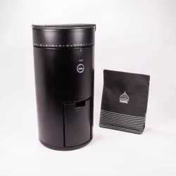 Černý elektrický mlýnek na kávu na bílém pozadí s balíčkem lázeňské kávy