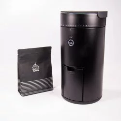 Černý elektrický mlýnek na kávu na bílém pozadí s balíčkem lázeňské kávy
