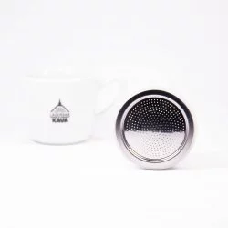 Stříbrné sítko do Bialetti moka konvice opřené o hranu na bílém pozadí s šálkem lázeňské kávy