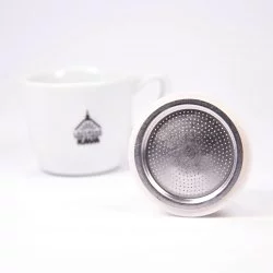 Hliníkové stříbrné těsnění do Bialetti moka konvice opřené o hranu na bílém pozadí s šálkem lázeňské kávy
