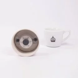 Detail na víčko keramické termosky ze spodní strany s lázeňskou kávou v pozadí.