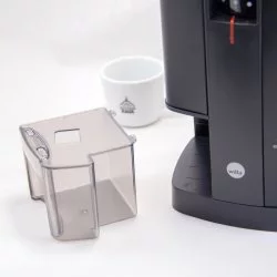Plastová násypka na elektrický mlýnek na kávu a bílým hrnkem značky Láeňské kávy v pozadí