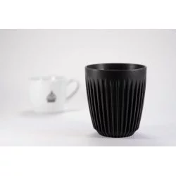 Černý ekologický hrnek Huskee na bílém pozadí s šálkem lázeňské kávy