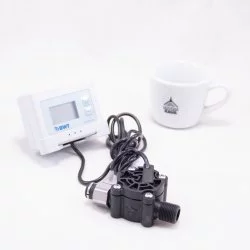 LCD displej značky BMWT AQA peo filtrování vody s čeerným kabelem na bíllém stole společně s šálkem značky Lázeňská káva na bílém pozadí
