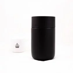 Černý termohrnek Fellow Carter s víčkem o objemu 235 ml na bílém pozadí s šálkem lázeňské kávy