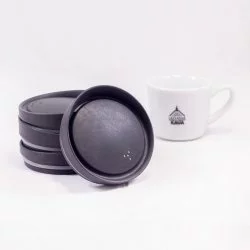 Černé ekologické víčko Huskee, 3 ks naskládané na sobě, jeden opřený o ně na bílém pozadí s šálkem lázeňské kávy