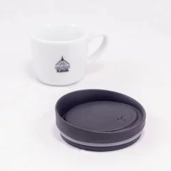 Černé ekologické víčko Huskee na bílém pozadí s šálkem lázeňské kávy