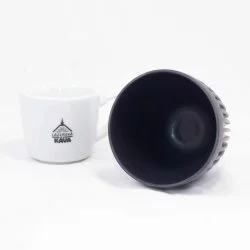 Černý ekologický kelímek Huskee položený na bílém pozadí s šálkem lázeňské kávy
