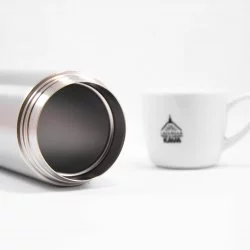 Položená termolahev Kinto bez víčka na bílém pozadí s šálkem lázeňské kávy
