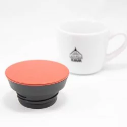 Detail na oranžové víčko termolahve Kinto na bílém pozadí s šálkem lázeňské kávy