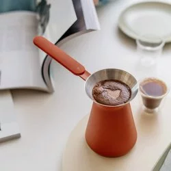 Džezva v cihlové barvě položená na stole s kávou
