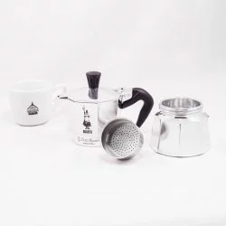 Rozložené části stříbrné Bialetti Moka Express konvice na bílém pozadí s šálkem lázeňské kávy
