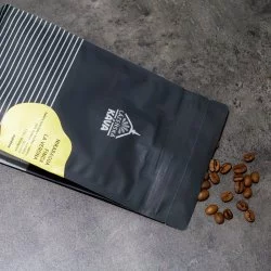 Balíček lázeňské kávy Nikaragua - Finca La Verona položený na šedé lince s rozsypanými kávovými zrny