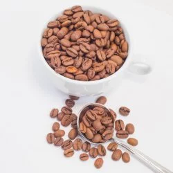 Čerstvě upražená kávová zrna v hrníčku a na stole