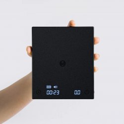 Ruka držící baristickou digitální váhu značky Black Mirror, pohled shora Ruka držící baristickou digitální váhu značky Black Mirror, pohled shora