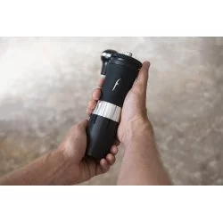 Ruce držící černý ruční mlýnek na kávu značky Flair Royale Grinder s násypkou kapacity 25g