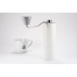 Ruční mlýnek na kávu bílé barvy značky Timemora C2 na bílém stole doplněný bílým šálkem s logem Lázeňské kávy