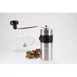 Stříbrný ruční mlýnek na bílém pozadí s šálkem lázeňské kávy a větvičkou