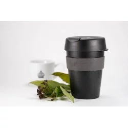 Černý plastový thermo hrnek s šedým držákem na bílém stole s rostlinou bílý hrnek značky Lázeňská káva s bílé pozadí