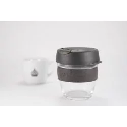 Skleněný termohrnek o objemu 227 ml s šedým víčkem a šedým gumovým držákem na bílém pozadí s šálkem lázeňské kávy